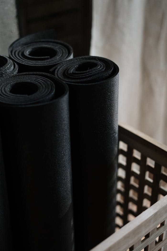 about-img Close-up view of black yoga mats rolled and stacked in a wooden basket indoors.
